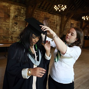A person helping a student with her graduation clothes 