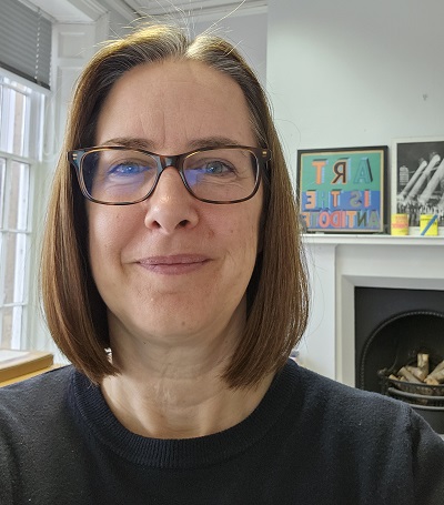 Image of a woman with straight brown bobbed hair and glasses with artwork behind her