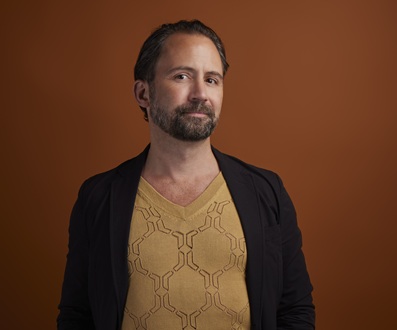 A head and shoulders shot of a man with dark hair and beard