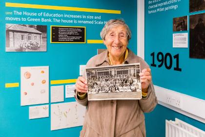An older woman holds up an image of her younger self at college