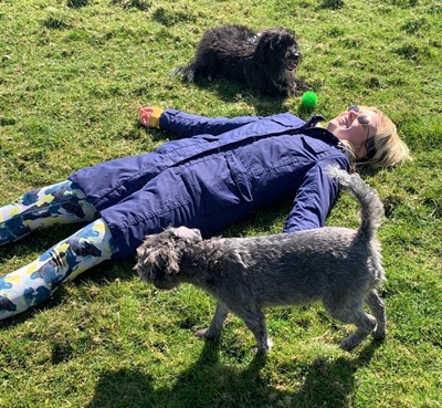 a woman in a blue coat lies on the grass with two dogs
