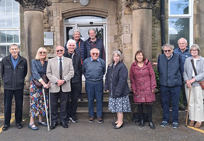 A group of former college staff posing in front of an old building