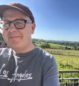 A man with glasses and a baseball cap in a green landscape