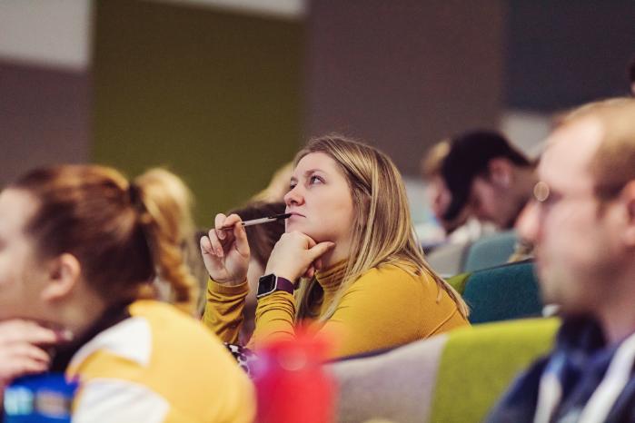 A room full of adults watch a lecture.