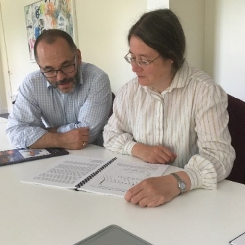 A man and woman sitting at a table reading a piece of text.