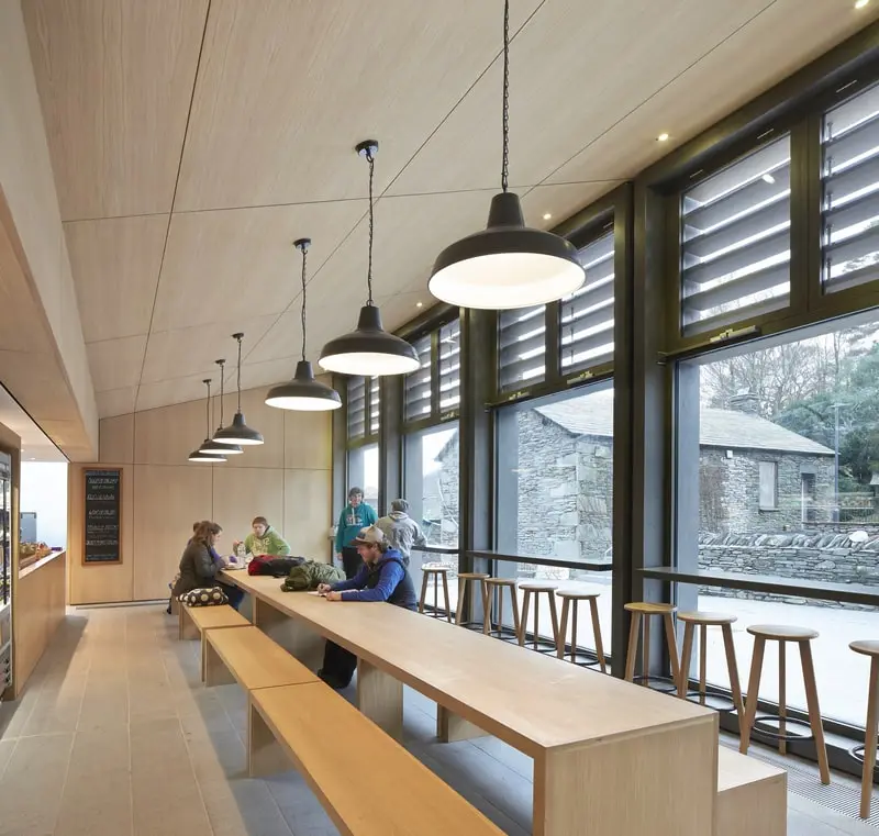 Several students eating and chatting at the far end of a long bench in a modern canteen.