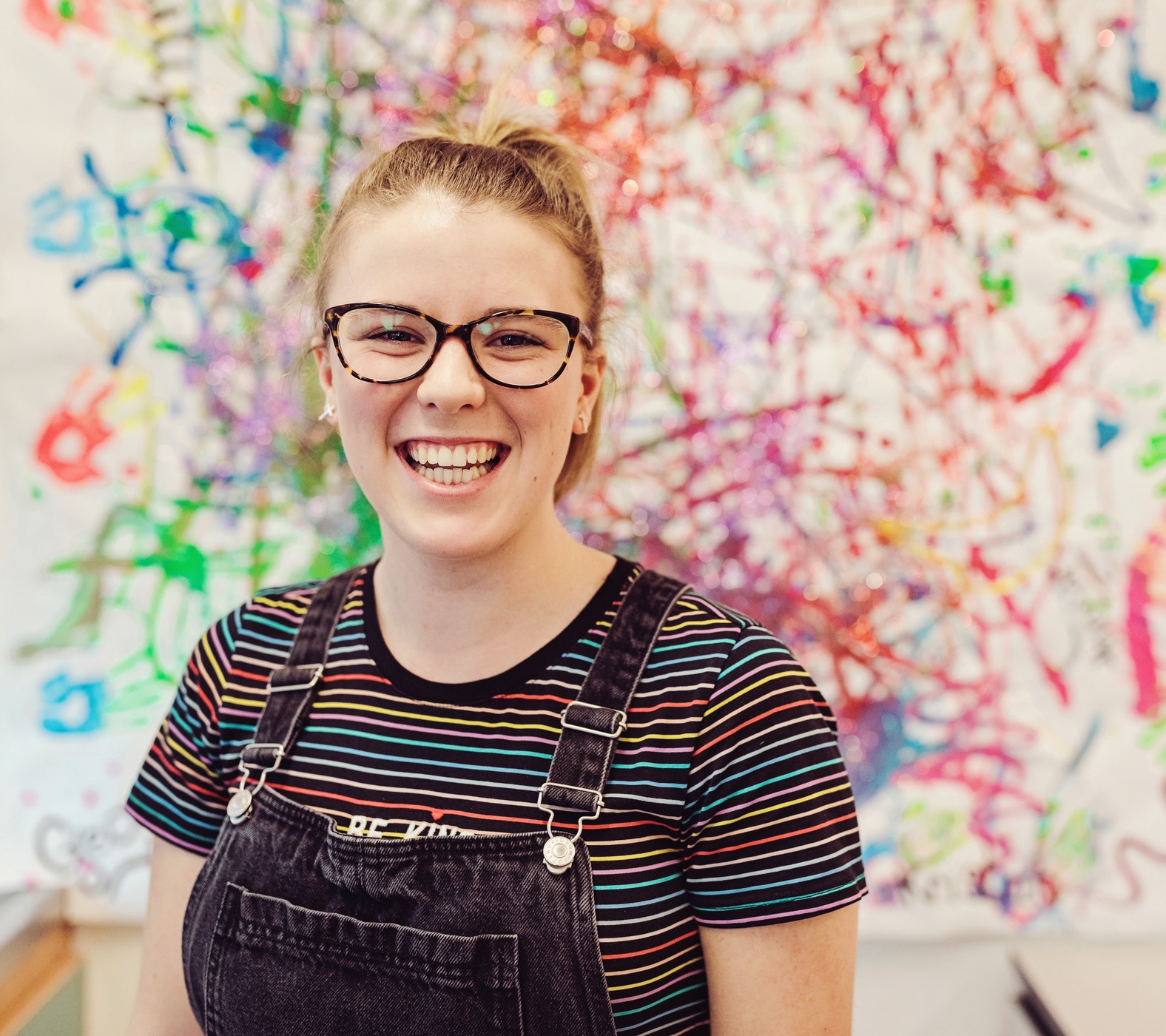 A student stands in front of a wall splattered with paint.