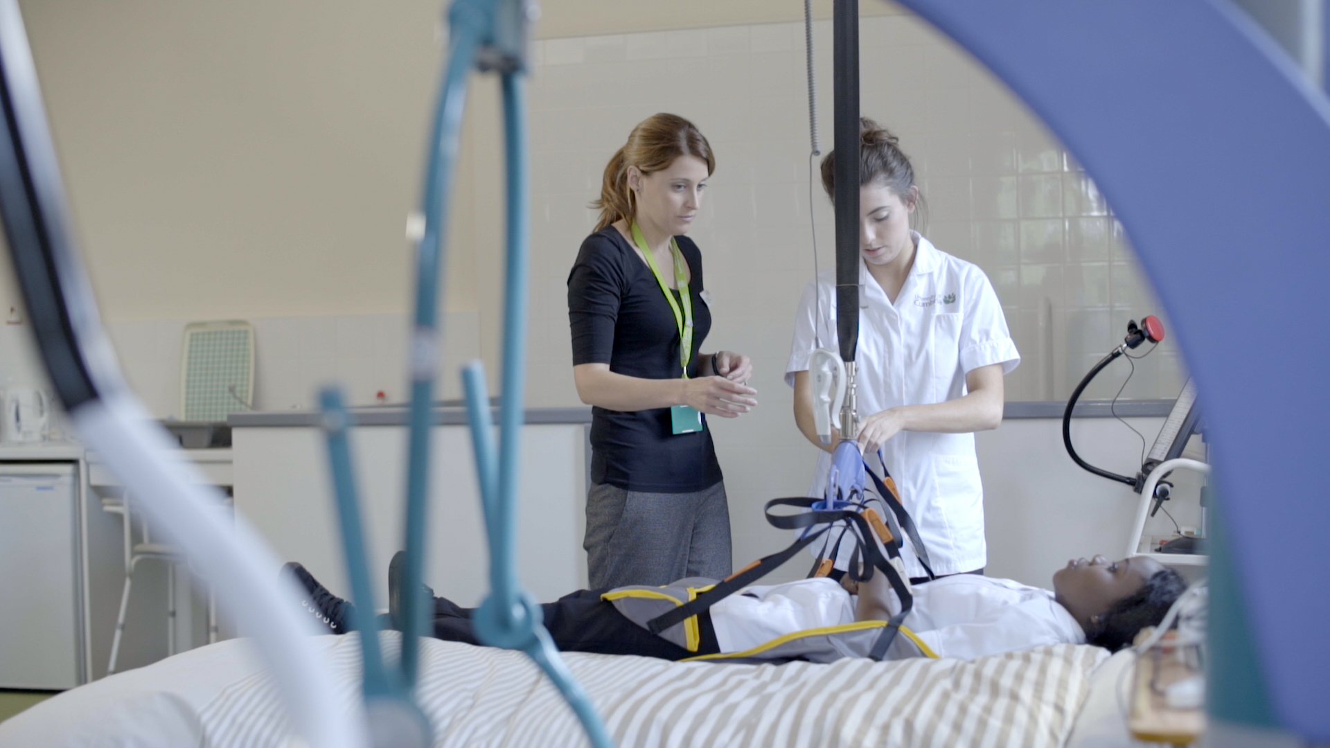 Occupational Therapy , Occupational Therapy - female student practising on another female student who is lying on a hospital bed, with lecturer watching over
