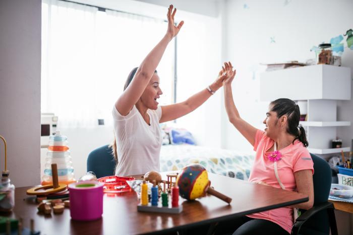 Learning Disability Nursing , female Learning Disability Nurse holding hands and smiling with a girl in a pink top