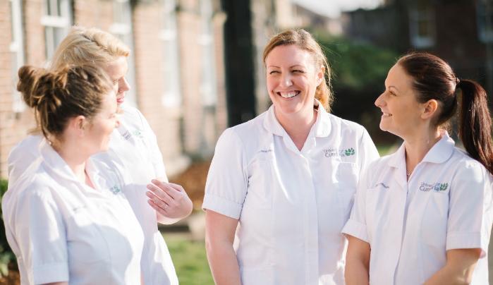 Adult Nurse, Four female nursing students wearing their university tunics standing in an open circle smiling and laughing with one another.