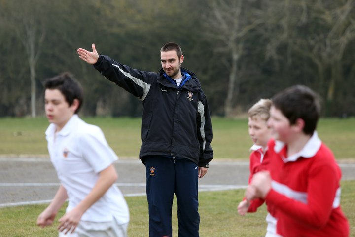 PE Sports School Teacher, male PE teacher pointing to the left and young male students running in that direction