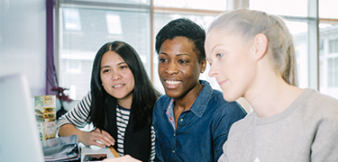 Three women sitting together working at a laptop.