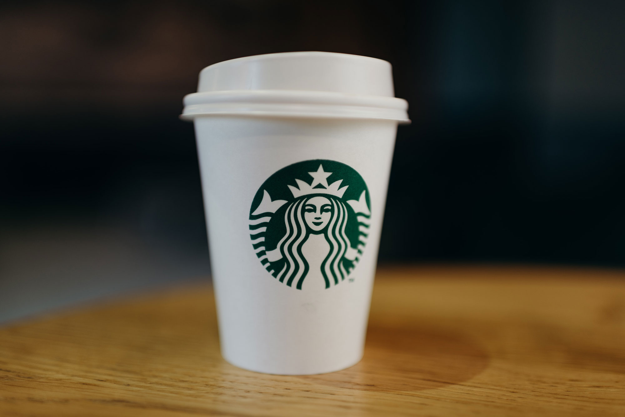 An extremely shallow focus close-up of a takeaway coffee cup with the Starbucks logo printed on the front.