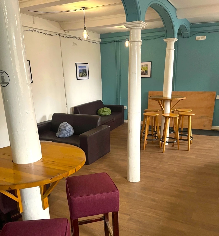 A small empty student bar in the day time. Fairy lights are strewn from the ceiling and a canoe is mounted on the red feature wall at the far end.