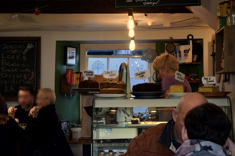 Ambleside Coffee Blog 7, Ambleside Coffee Blog: A photo of a cafe that serves a variety of cakes. There are also people sat enjoying their hot drinks and socialising.