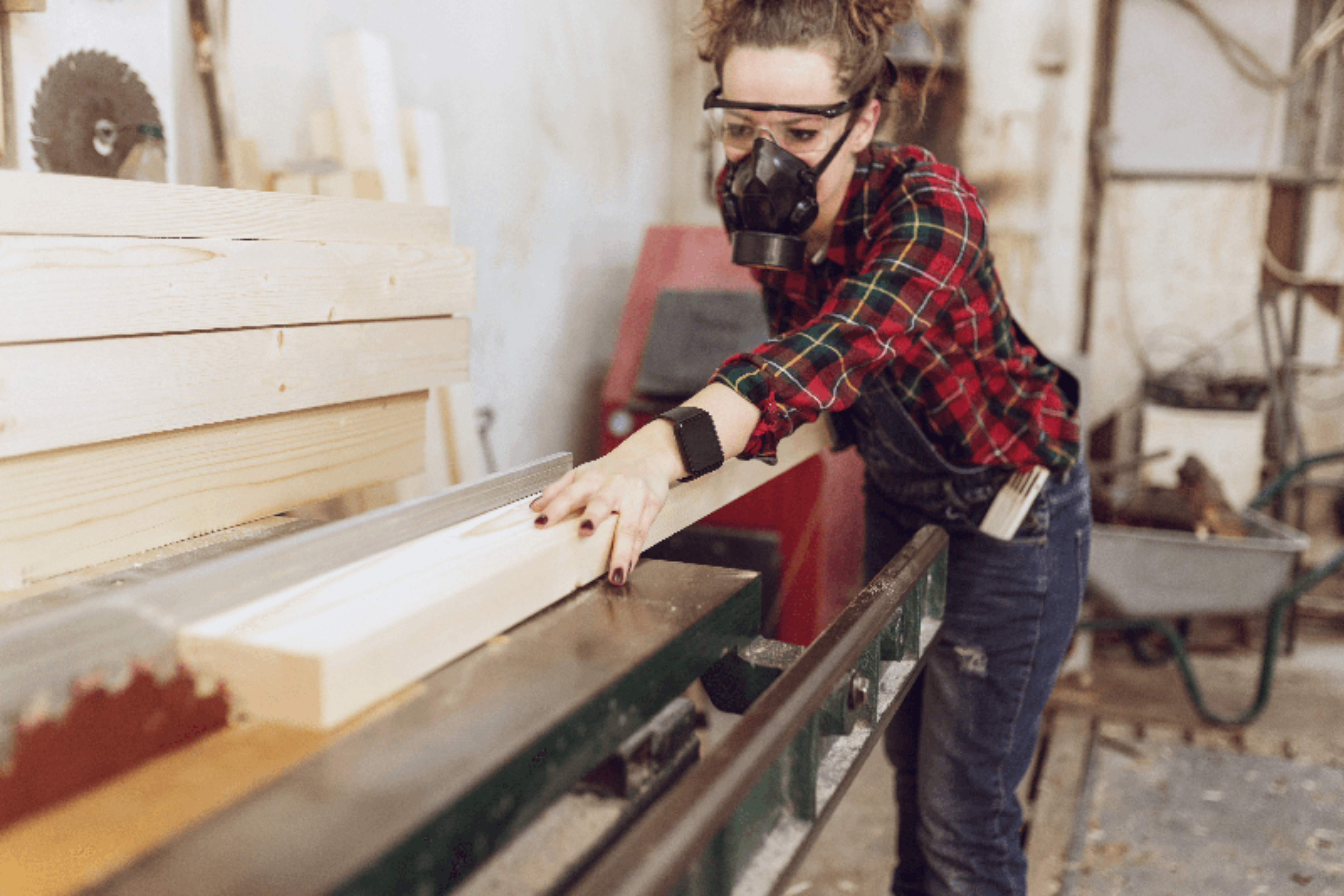 A female joiner using a saw in a workshop, A female joiner wearing a dust mask and safety glasses using a circular bench saw to cut timber. 