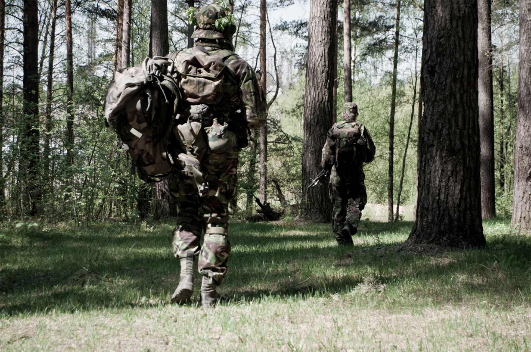 Two people walking through the woods in army camouflage uniform, Two people walking through the woods in daylight, dressed in army camouflage and carrying weapons. 