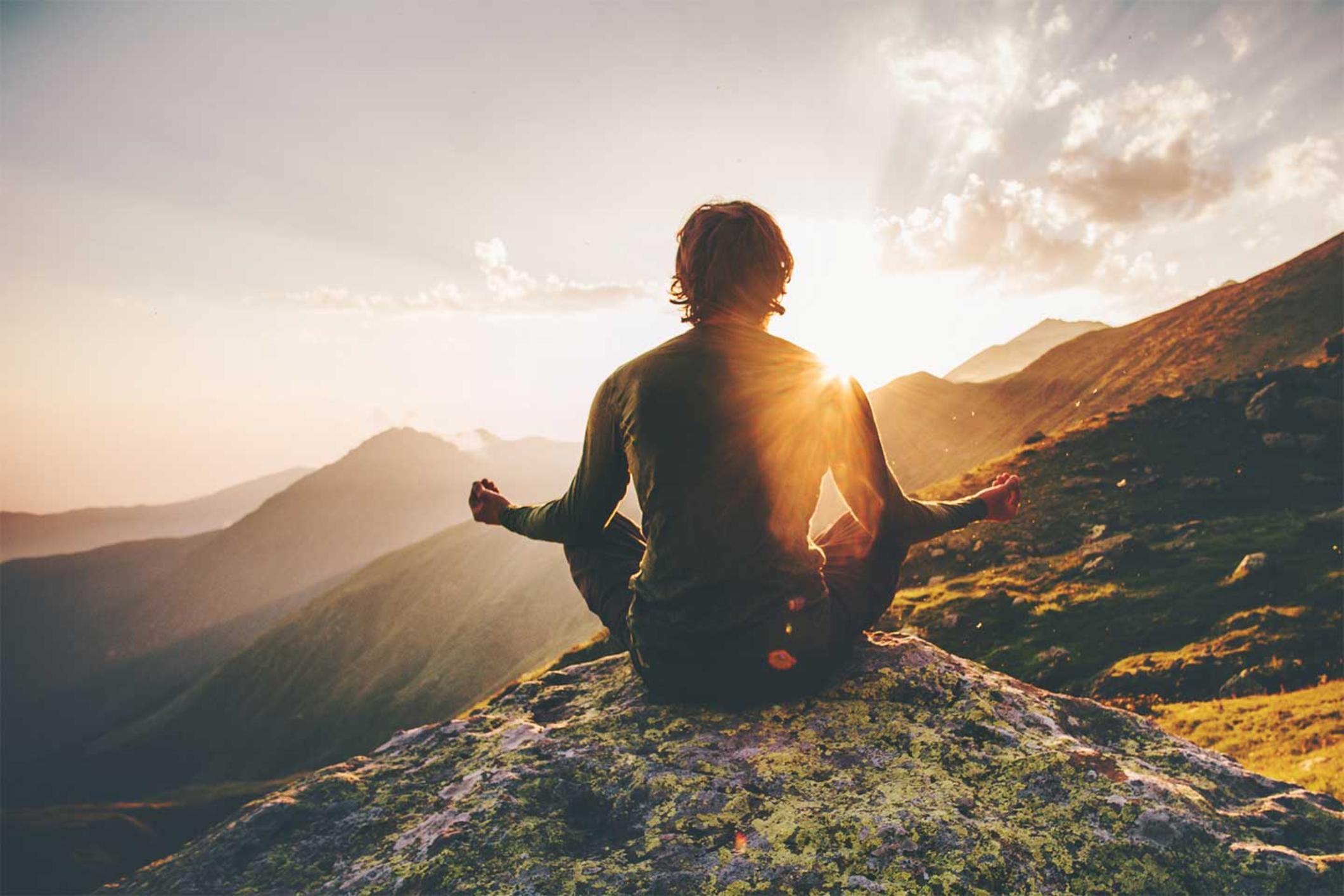 Person meditating on a hilltop, Person sitting cross-legged on a hilltop meditating at sunrise. 
