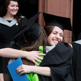 A photo of two female students hugging and celebrating during a graduation ceremony