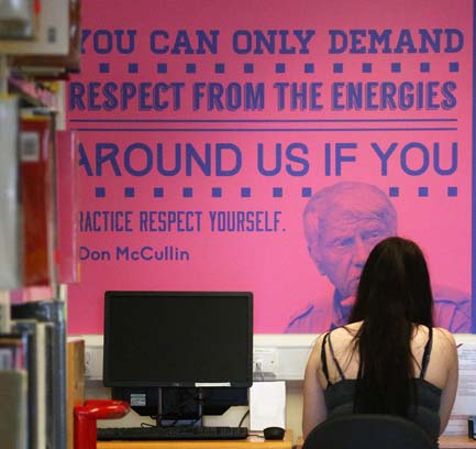 A female student working beside a computer in a library with an inspirational quote on the wall in front of her.