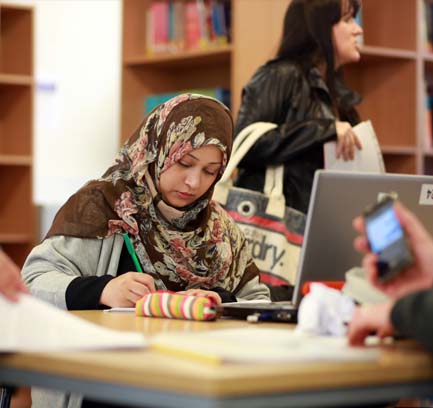 A woman writing notes at a table in a library.