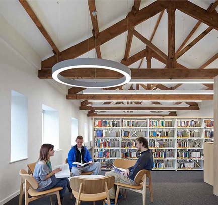 Three students holding books and having a conversation while sitting around a small, low table in a library.