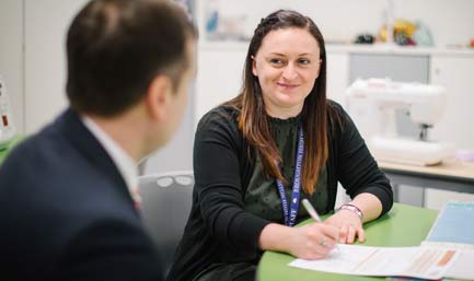 A photo of two people talking while filling in a form.