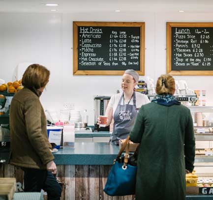 A barista serves two customers with a cup of coffee from behind the counter of a canteen.