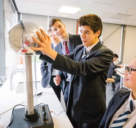 A photo of a group students in a science lab with an amazed expression on their face while interacting with a piece of science equipment.
