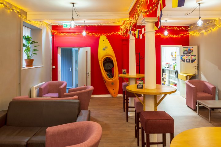 A small empty student bar in the day time. Fairy lights are strewn from the ceiling and a canoe is mounted on the red feature wall at the far end.