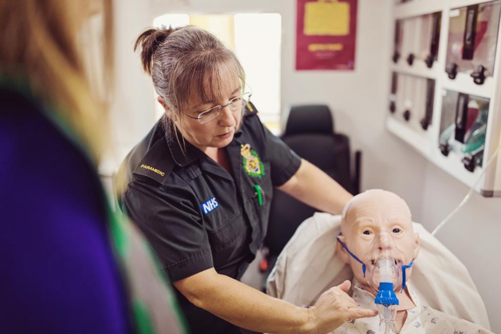 A nurse attaches a breathing tube to a mannequin. 