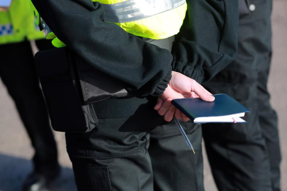 A police officer holds a note pad behind their back.