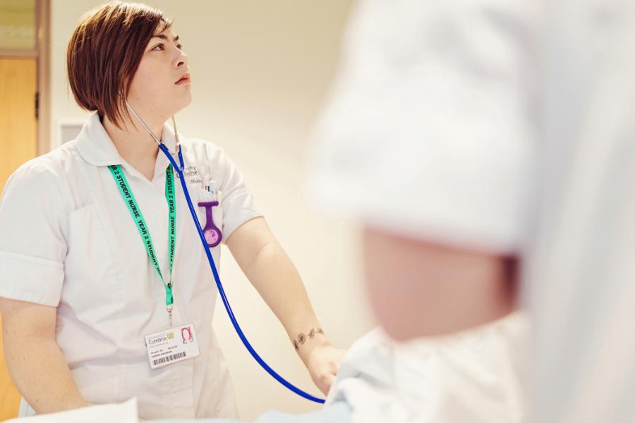 A student nurse checks a dummy's vitals.