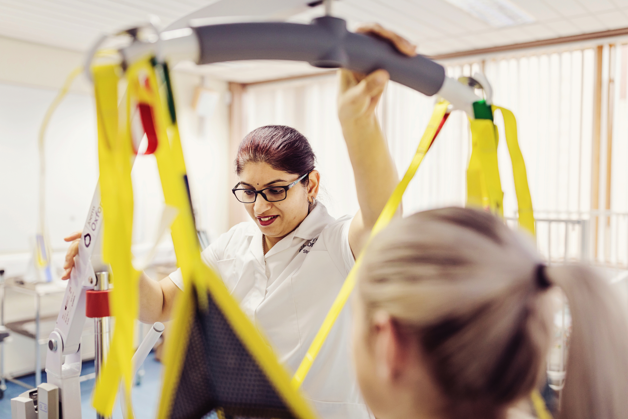 A nursing student uses assistive lifting tech to support a model patient.