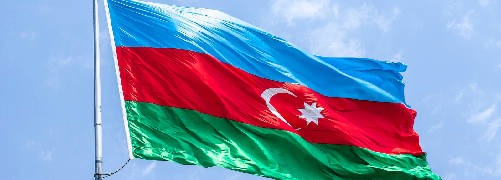 A picture of a flag pole with the Azerbaijan flag at the top, blowing in the wind.