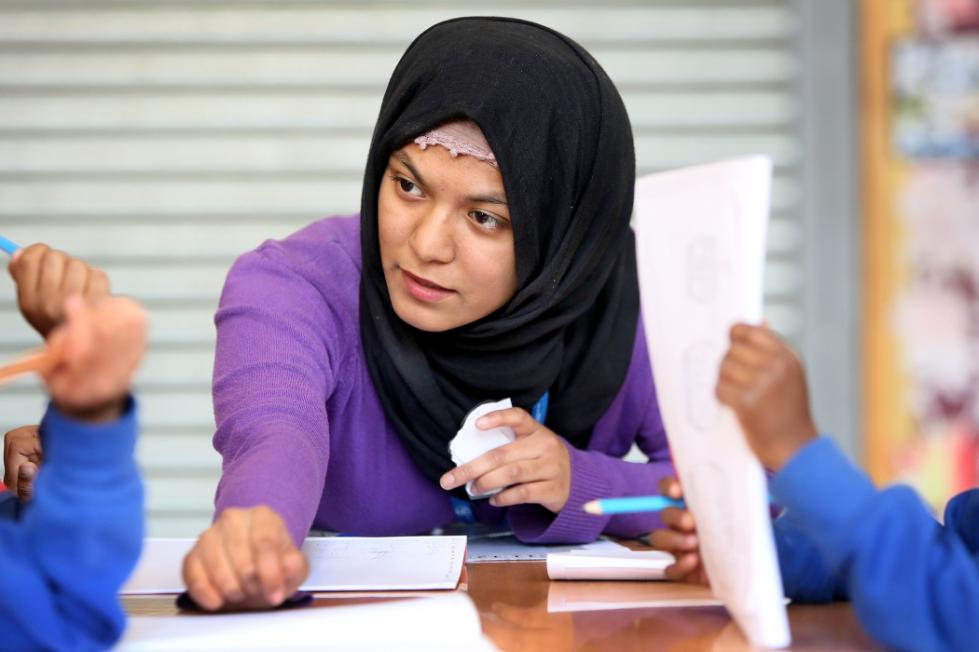 A teacher leans over the table to help a student.