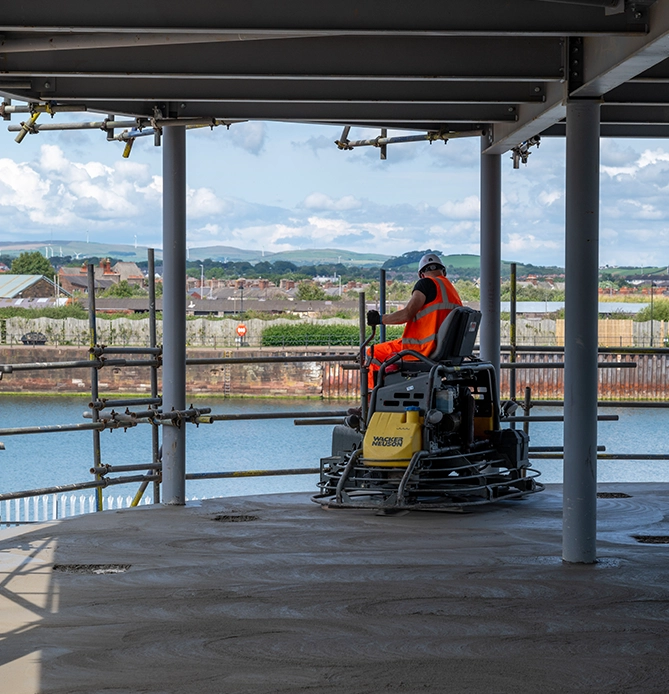 A workman driving a piece of machinery working on the University of Cumbria Barrow campus under construction in 2024